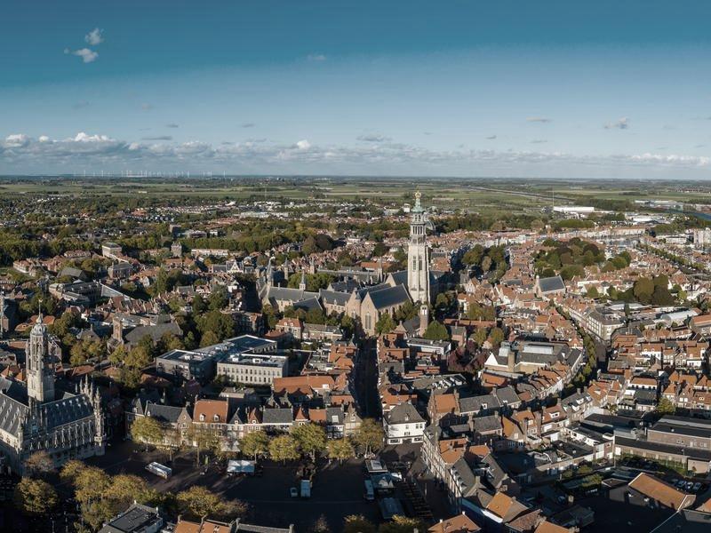 A Dutch town from the air, a tall church tower over red rooftops with wind turbines on the flat horizon