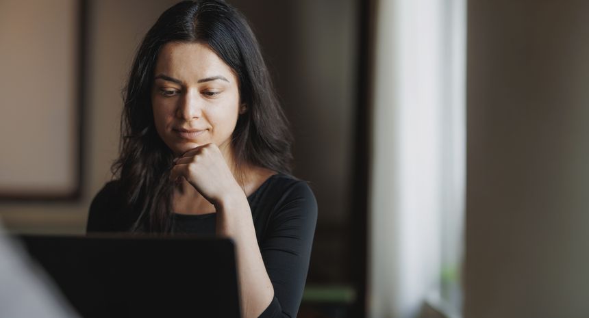A woman reading from a laptop by a window